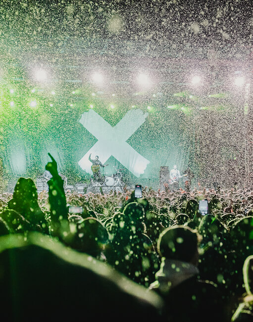 Konzert mit Publikum, grüner Bühne, großem X und Konfetti.