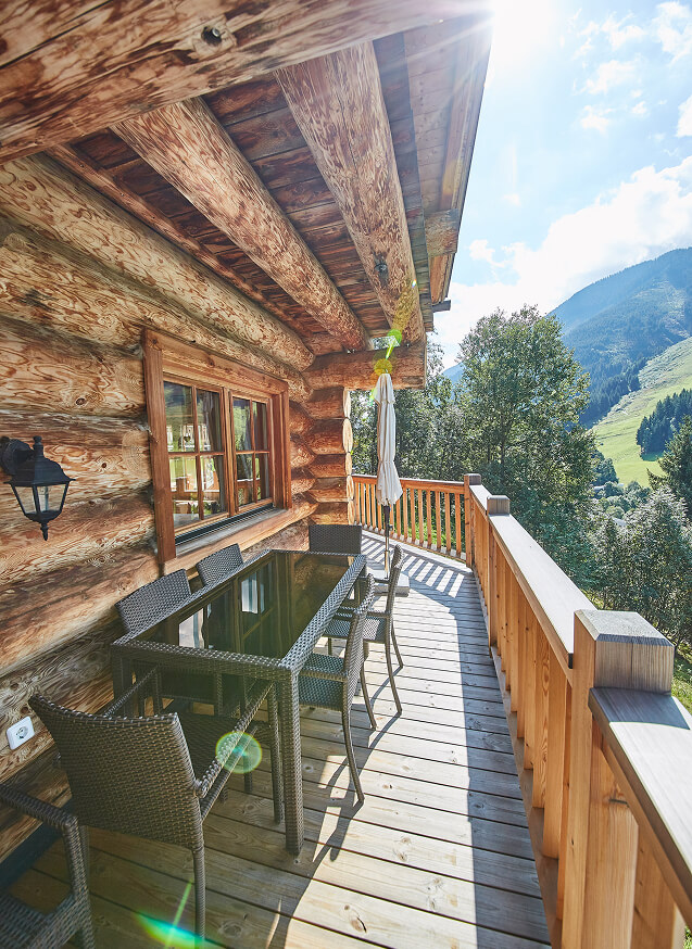 Sonniger Blockhaus-Balkon mit Esstisch und Bergsicht.