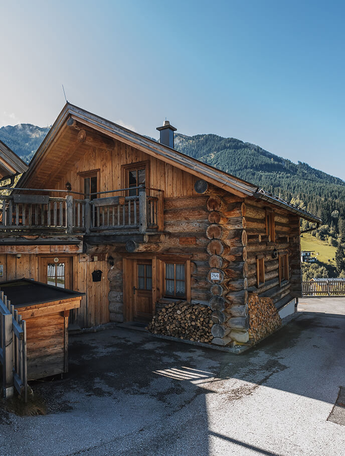 Sonniges Blockhaus mit Balkon vor bewaldeten Bergen.