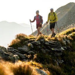 Zwei Wanderer mit Trekkingstöcken in felsiger Berglandschaft.