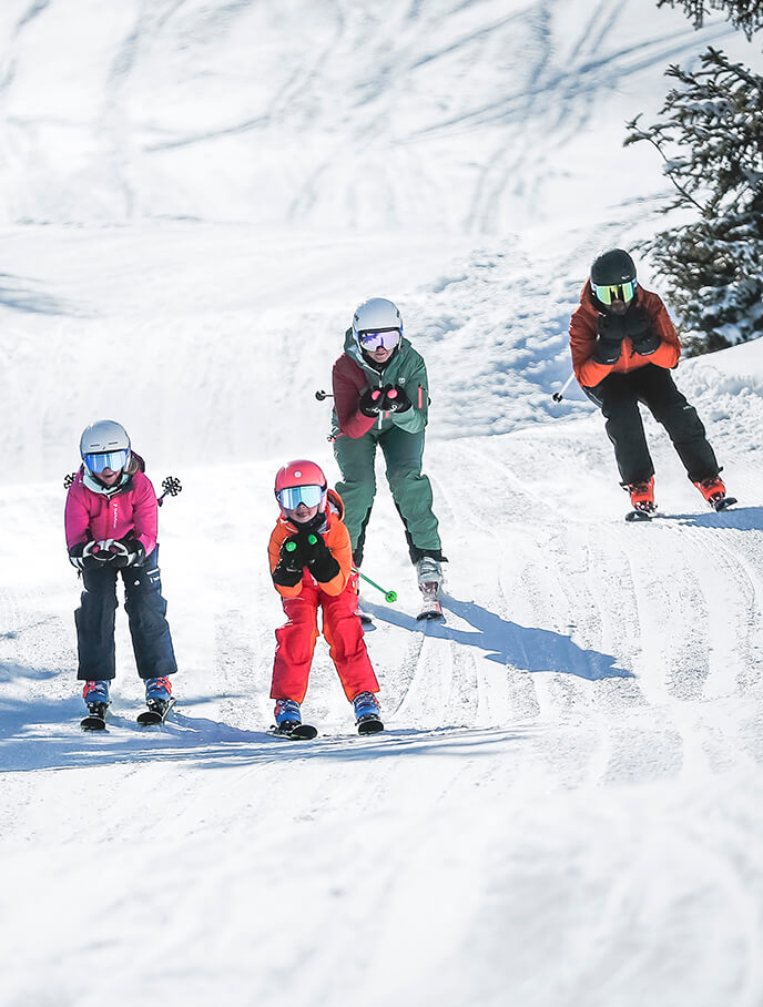 Vier Skifahrer, davon zwei Kinder, auf verschneiter Piste.
