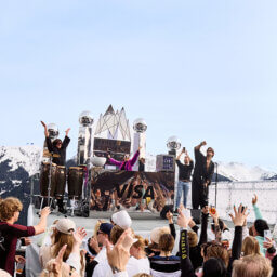 Zuschauer feiern bei Outdoor-Konzert vor schneebedeckten Bergen.