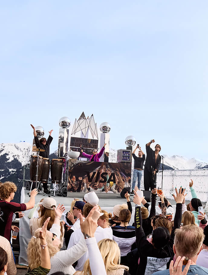 Zuschauer feiern bei Outdoor-Konzert vor schneebedeckten Bergen.